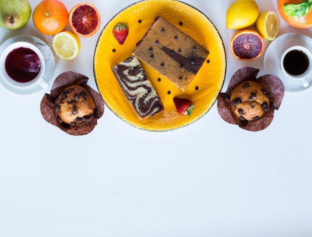 Faccia colazione con caffè e tè con differenti pasticcini e frutti su una tavola di legno bianca