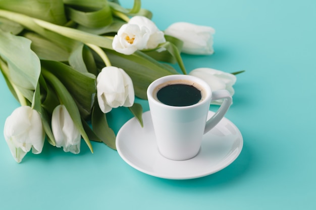 Faccia colazione con la tazza di caffè e i tulipani bianchi sulla pianura