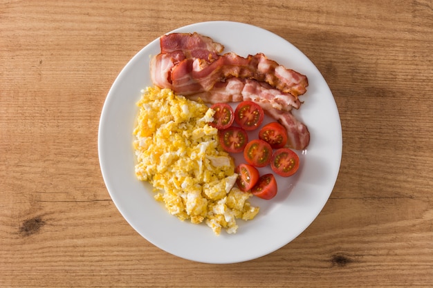 Faccia colazione con le uova, la pancetta affumicata ed i pomodori rimescolati sulla vista di legno del piano d'appoggio