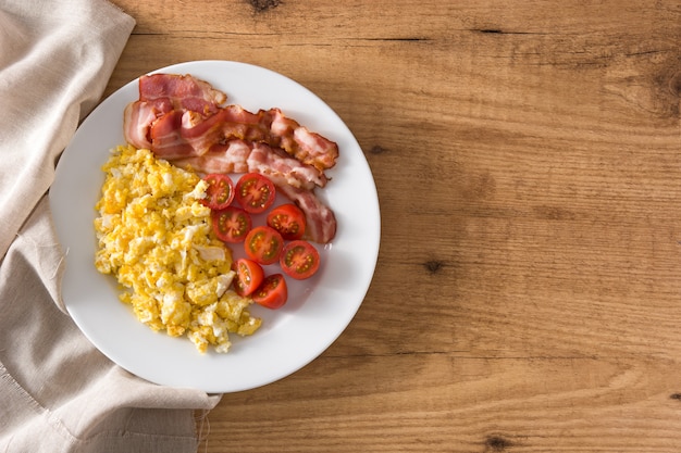 Faccia colazione con le uova, la pancetta affumicata ed i pomodori rimescolati sullo spazio di legno della copia di vista del piano d'appoggio