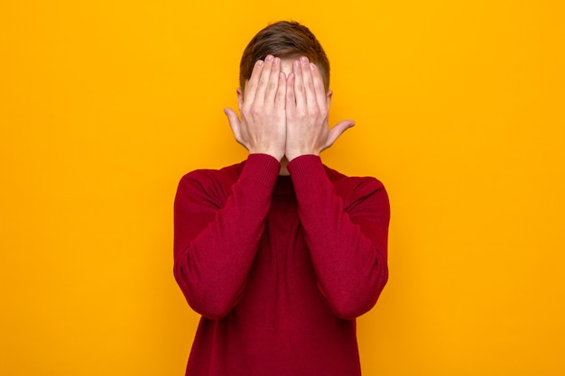 Faccia coperta di mani giovane bel ragazzo che indossa un maglione rosso