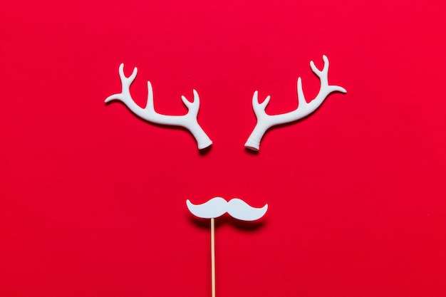 Faccia di renna festiva fatta di corna bianche e baffi bianchi su sfondo rosso