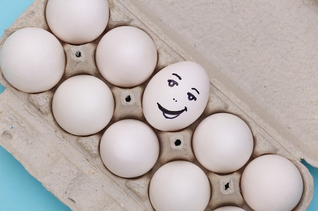 Faccia felice dell'uovo nel vassoio delle uova su priorità bassa blu. Vista dall'alto