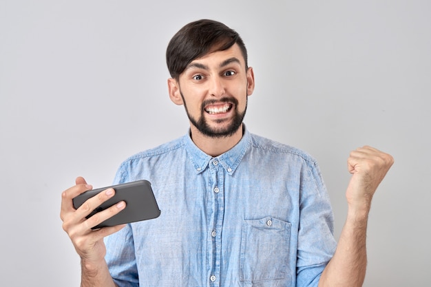 Faccia felice uomo fortunato che tiene il telefono cellulare in mano e celebra la vendita della vittoria isolato su sfondo bianco studio