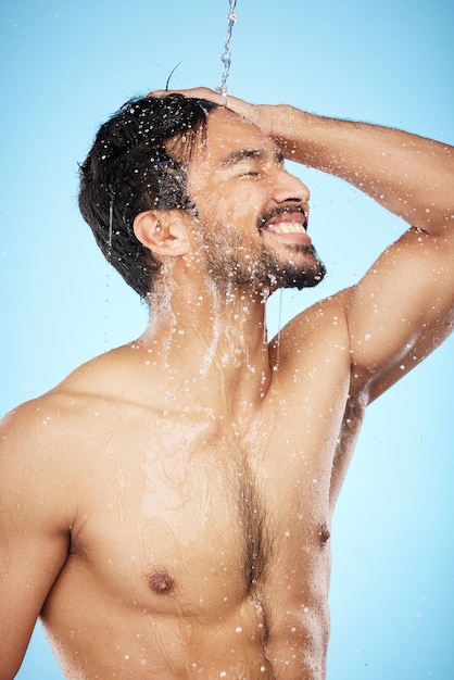 Faccia spruzzi d'acqua e uomo nella pulizia della doccia per la cura del corpo in studio isolato su sfondo blu Cura della pelle igienica e profilo del modello maschile che fa il bagno e si lava per la salute, il benessere e la bellezza