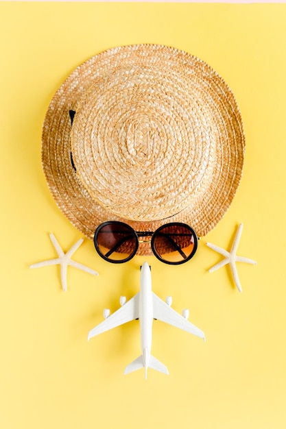 Faccia turistica fatta di cappello di paglia modello aereo aereo e occhiali da sole su sfondo giallo Concetto di accessori per viaggiatori