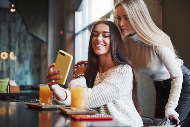 Facciamo una foto. Nel ristorante. Due amiche siedono al chiuso con drink giallo e usano lo smartphone