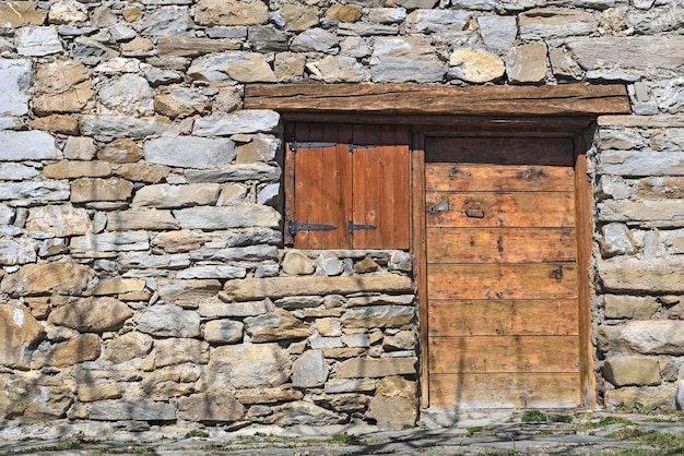 Facciata di vecchio chalet alpino in pietra con porta in legno e persiane chiuse