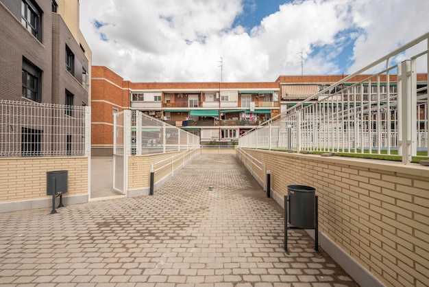 Facciate di case residenziali urbane con giardini e passerelle comunali con pavimentazioni in granito a terra e pareti in mattoni chiari in una giornata di sole con molte nuvole