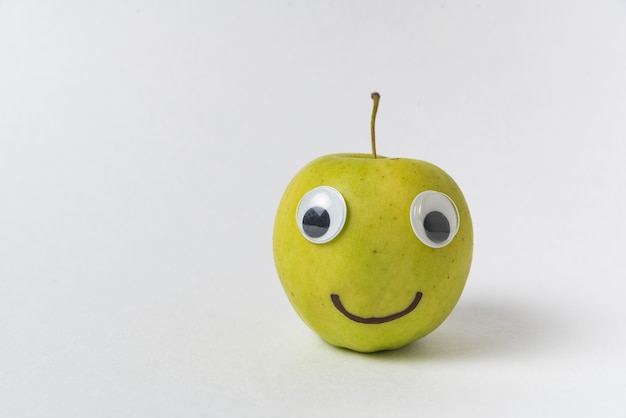 Faccina di mela su sfondo bianco. Mela con gli occhi Googly e sorriso disegnato.