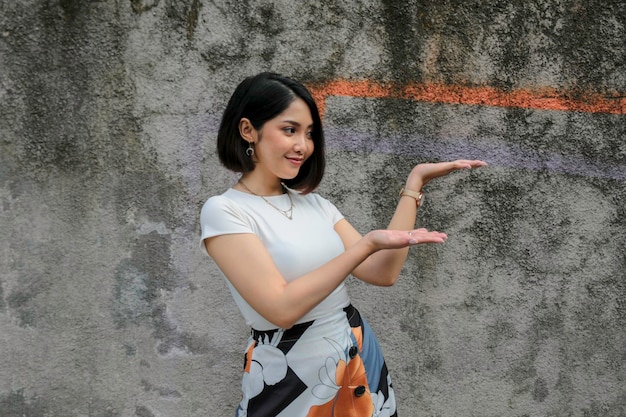 Faccina felice e sorridente con il sorriso di una giovane ragazza asiatica con la punta della mano sullo spazio vuoto