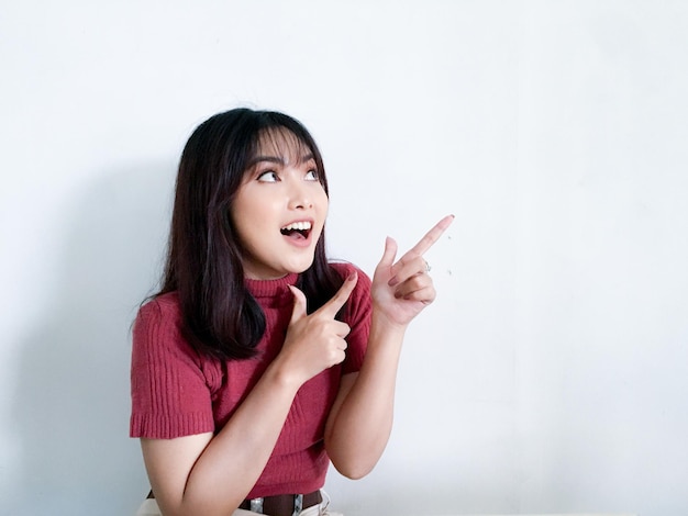 Faccina felice e sorridente con il sorriso di una giovane ragazza asiatica in camicia rossa con la punta della mano sullo spazio vuoto