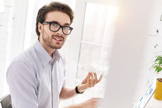 Facendo del mio meglio. Abile manager barbuto seduto al tavolo e lavorando sul suo laptop