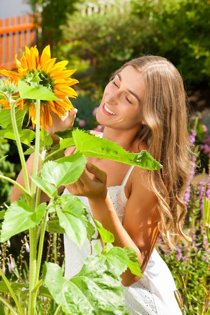 Facendo il giardinaggio in estate - donna felice con i fiori del sole nel suo giardino