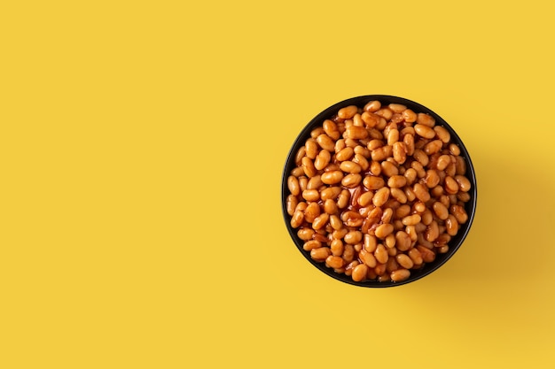 Fagioli bianchi in salsa di pomodoro in ciotola su sfondo giallo