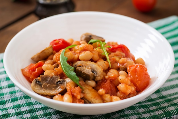 Fagioli bianchi in umido con funghi e pomodori con salsa piccante in una ciotola bianca