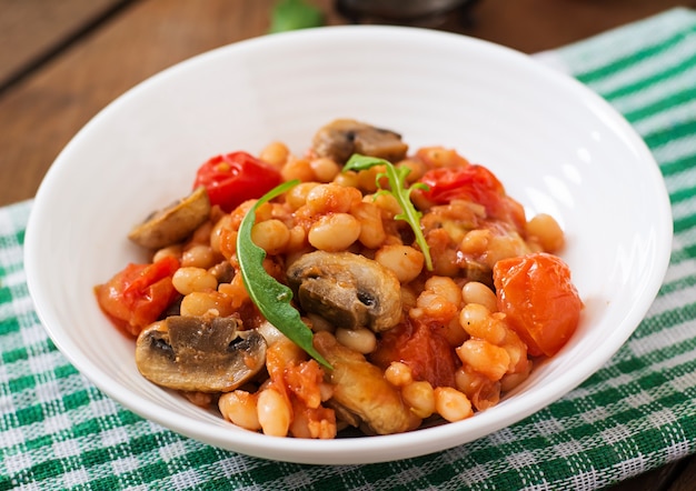 Fagioli bianchi stufati con funghi e pomodori con salsa piccante in una ciotola bianca