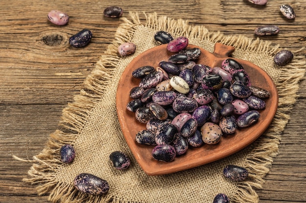 Fagioli multicolori assortiti in una ciotola di ceramica. Ingrediente sano crudo per cucinare cibo utile. Vecchio tavolo in legno, copia spazio