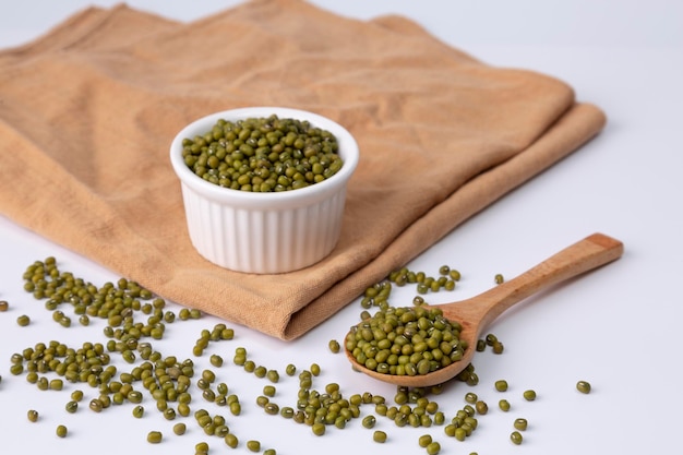 Fagiolo verde in una ciotola bianca su stoffa e cucchiaio di legno su sfondo bianco girato in studio