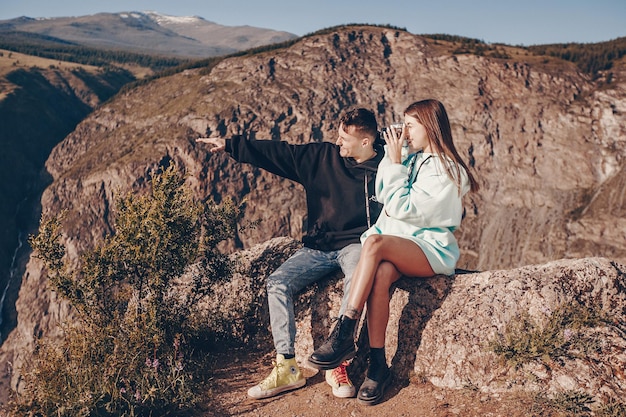 Fai un servizio fotografico turistico in montagne rocciose sotto un cielo spazioso. Un ragazzo e una ragazza sono seduti uno accanto all'altro su una roccia e cercano un angolo per una foto. La ragazza tiene la macchina fotografica tra le mani.