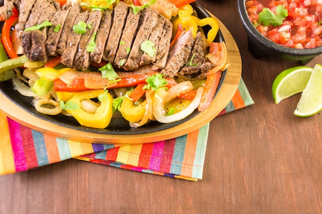 Fajitas di bistecca con peperoni e cipolla gialla su una padella per fajita in ghisa.