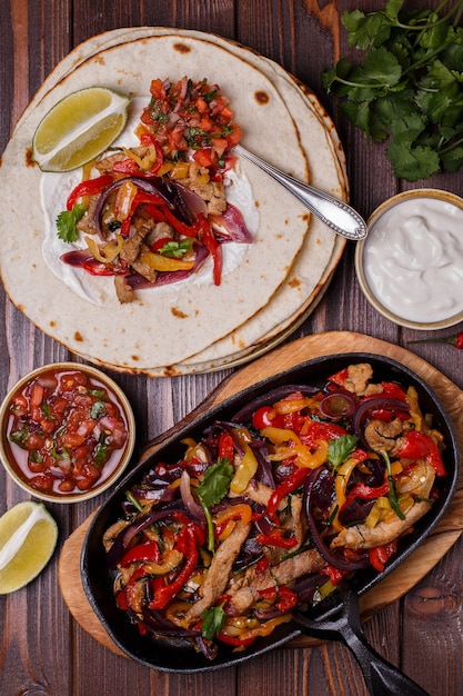 Fajitas di maiale con cipolle e pepe colorato, servite con tortillas, salsa e panna acida.