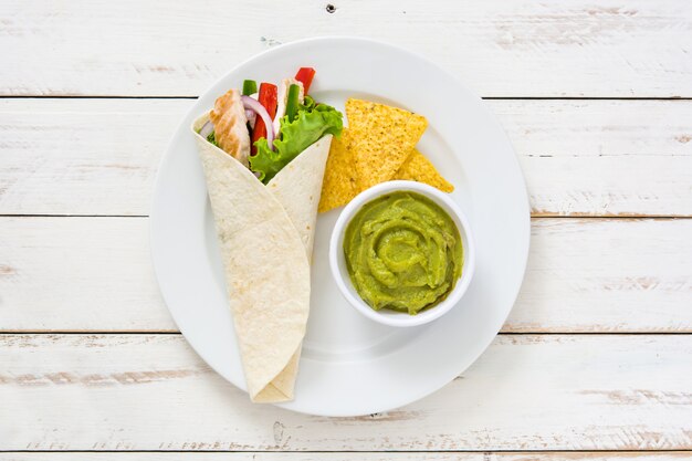 Fajitas di pollo messicano con salsa guacamole su un piatto e un tavolo di legno bianco