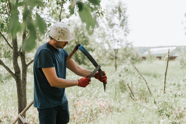 Falciare l'erba tradizionale vecchio stile con la falce a mano nella fattoria del villaggio domestico giovane contadino maturo che affila la falce con erba o cote per falciare l'erba coltivata di un terreno agricolo