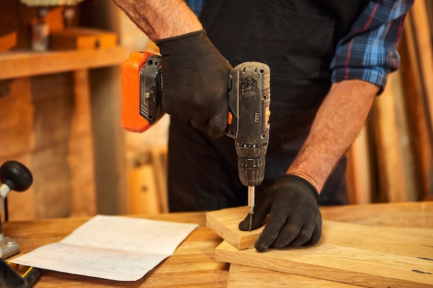 Falegname anziano con strumento di perforazione che lavora nell'officina di falegnameria per realizzare un mobile