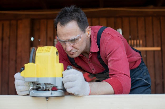 Falegname artigiano lavora sul pezzo in legno con utensile di fresatura si chiuda al laboratorio di cottage