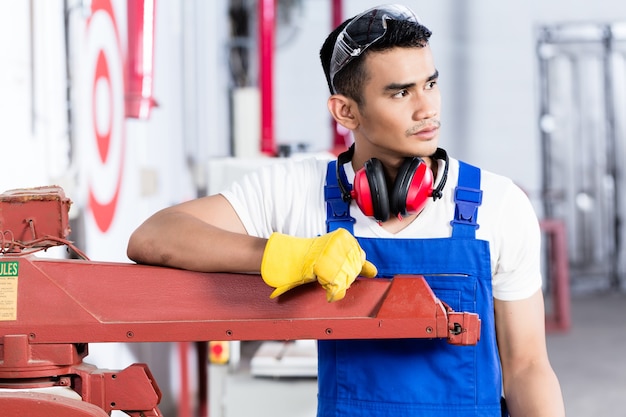 Falegname asiatico con sega elettrica in officina in piedi su una macchina