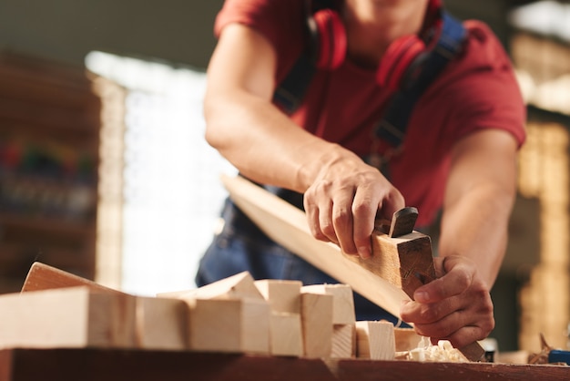 Falegname professionista che leviga accuratamente la tavola di legno con pialla a mano