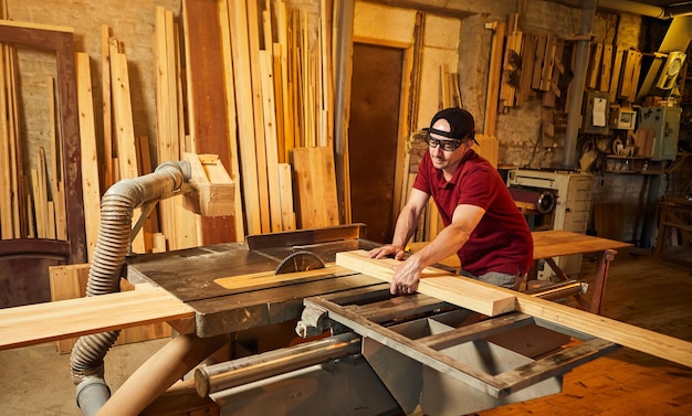 Falegname professionista in uniforme lavora su una macchina per la lavorazione del legno presso la falegnameria