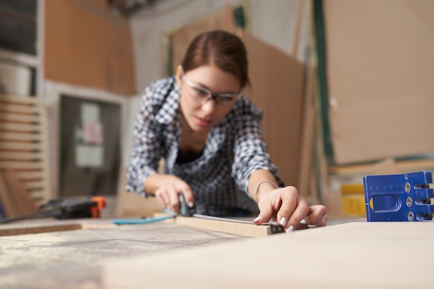 Falegname ragazza con tavola di legno dietro il banco di lavoro in officina