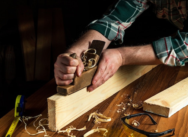 Falegname utilizzando una pialla a mano per pulire una tavola di legno. Mani del primo piano maestro al lavoro.