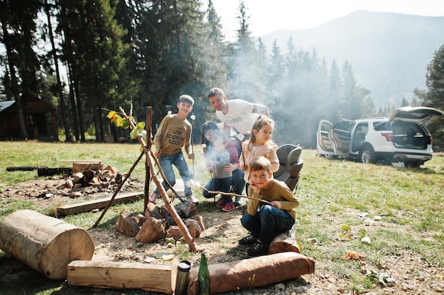 Falò di famiglia in montagna. Quattro bambini in campeggio. Marshmallow per barbecue. Escursione autunnale e clima del campo. Riscaldare e cuocere vicino alla fiamma insieme.