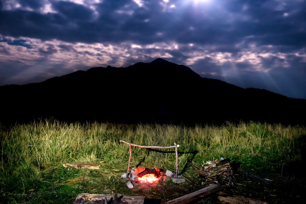 Falò sul prato verde vicino alla montagna di notte con cielo scuro e luce lunare