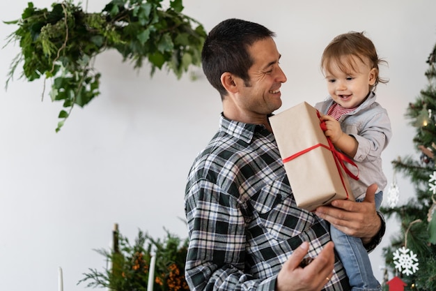 Famiglia a Natale a casa papà che dà al bambino una confezione regalo al mattino Papà tiene un ragazzino nel soggiorno Concetto di Capodanno a casa