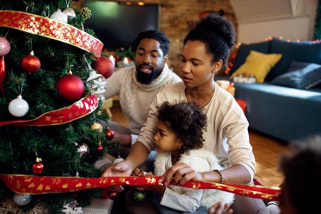 Famiglia afroamericana che si diverte mentre decora l'albero di Natale a casa