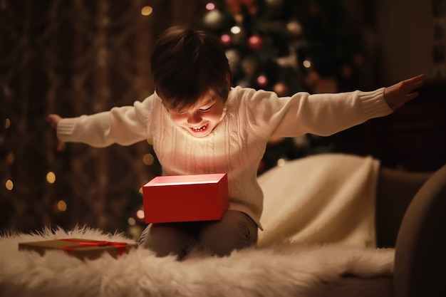Famiglia alla vigilia di Natale al caminetto. I bambini aprono i regali di Natale. Bambini sotto l'albero di Natale con scatole regalo. Soggiorno decorato con camino tradizionale. Serata d'inverno calda e accogliente a casa.