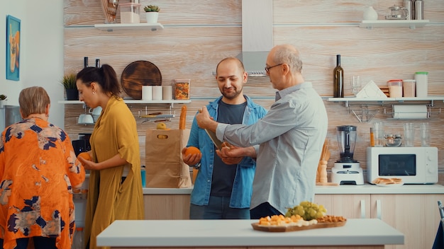 Famiglia allargata che mette la spesa in frigo. Giovane coppia proveniente dallo shopping portando un sacchetto di carta con generi alimentari, cibo fresco dal supermercato a casa dei genitori per preparare la cena in famiglia