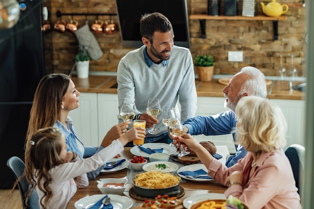 Famiglia allargata felice che parla mentre pranza e brinda al tavolo da pranzo