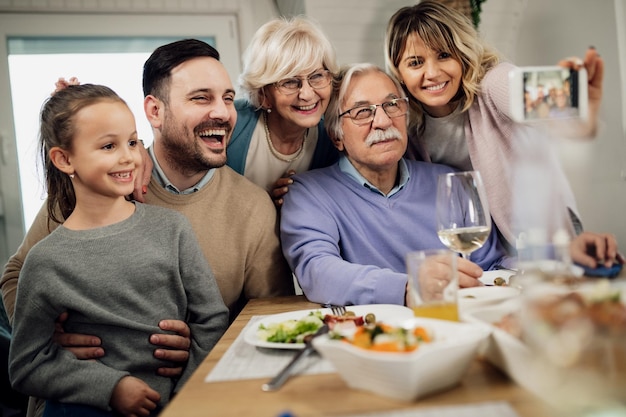 Famiglia allargata felice che si diverte mentre si fa selfie con lo smartphone al tavolo da pranzo