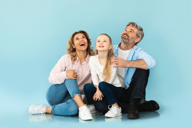 Famiglia allegra che osserva in su seduto e abbracciando su sfondo blu