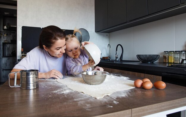 Famiglia amorevole felice che cucina insieme panetteria. Madre e figlia cucinano i biscotti e si divertono in cucina. Cibo fatto in casa e un piccolo aiutante.