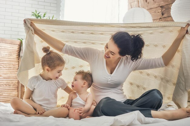 Famiglia amorevole felice. Madre e figlie bambine che giocano a letto.