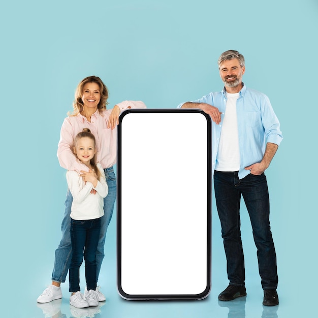 Famiglia appoggiata su un grande smartphone con sfondo blu schermo vuoto