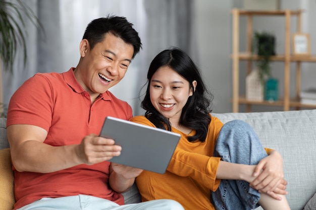 Famiglia asiatica allegra che si siede sul divano a casa usando il pad