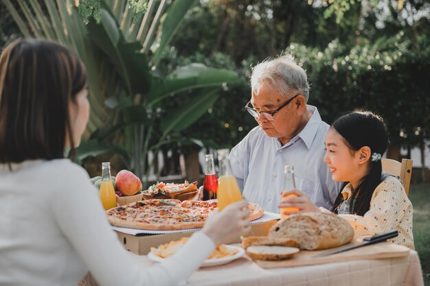 Famiglia asiatica che mangia pizza in giardino a casa. Genitore con stile di vita bambino e nonno in cortile.