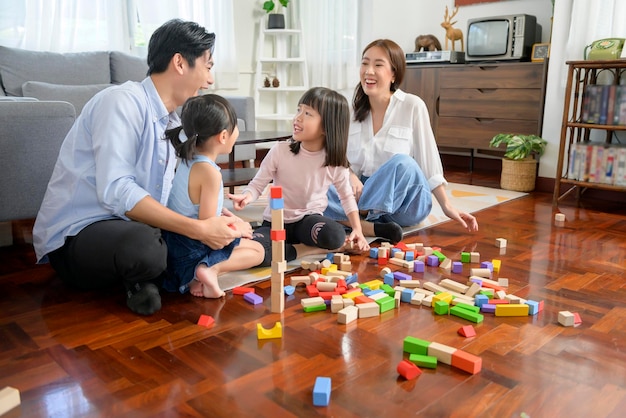 Famiglia asiatica con bambini che giocano e costruiscono una torre di blocchi di giocattoli in legno colorati in soggiorno